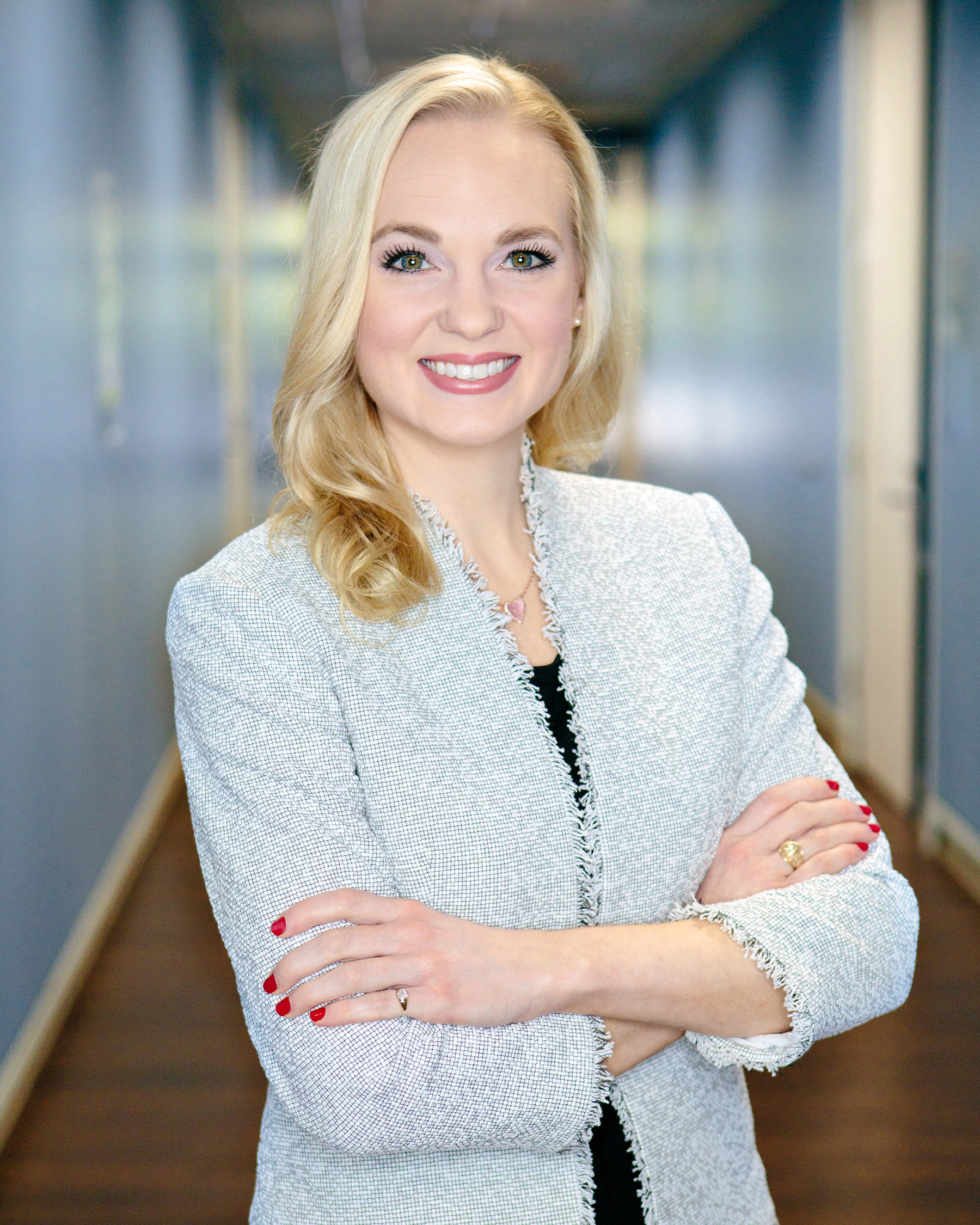 Dr Hadley Stevens Smith stands in a blue hallway, arms crossed, smiling at the camera